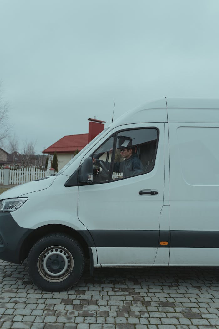 Driver in a white van parked on a suburban cobblestone street.